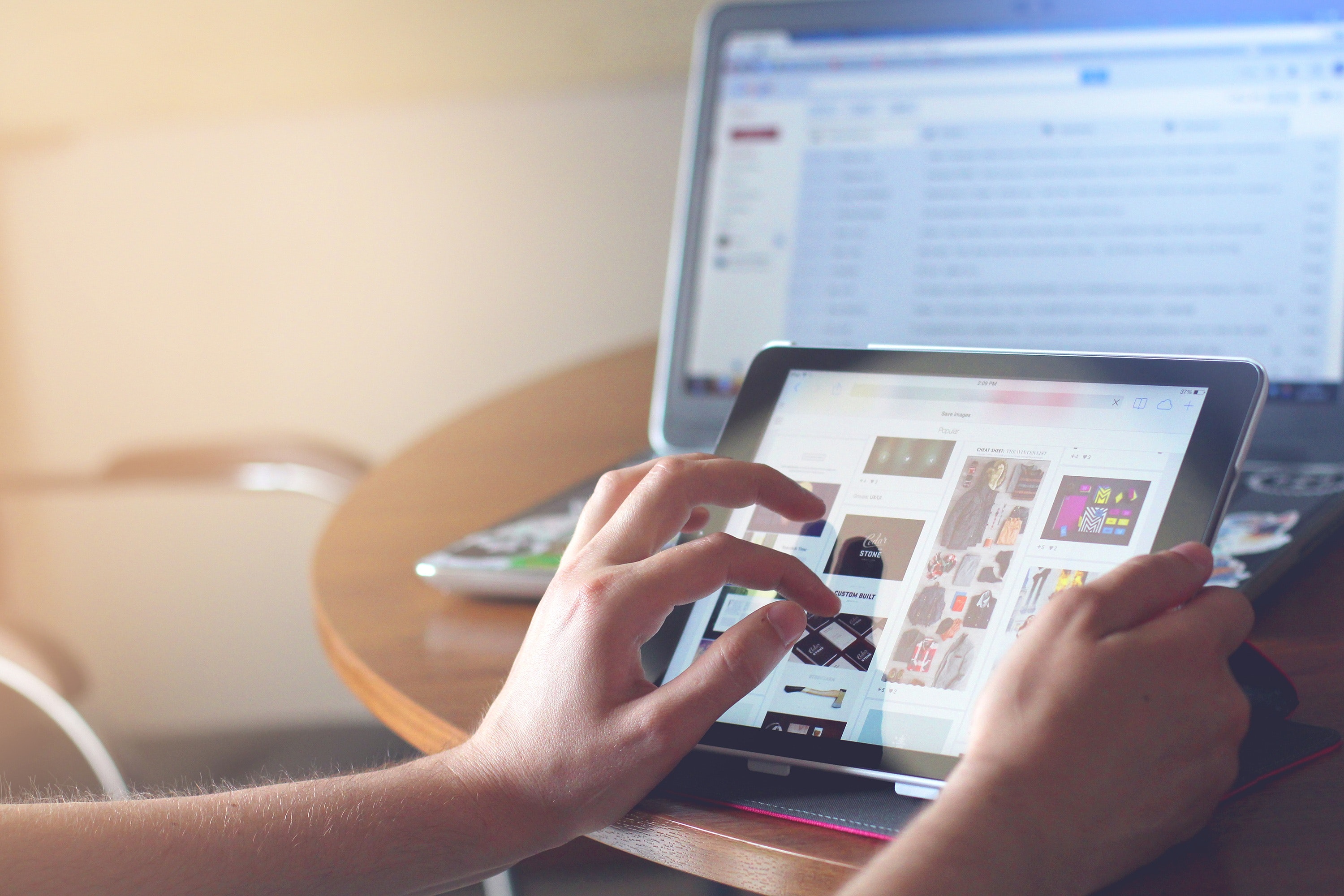 Person working a iPad Tablet and laptop on in the background