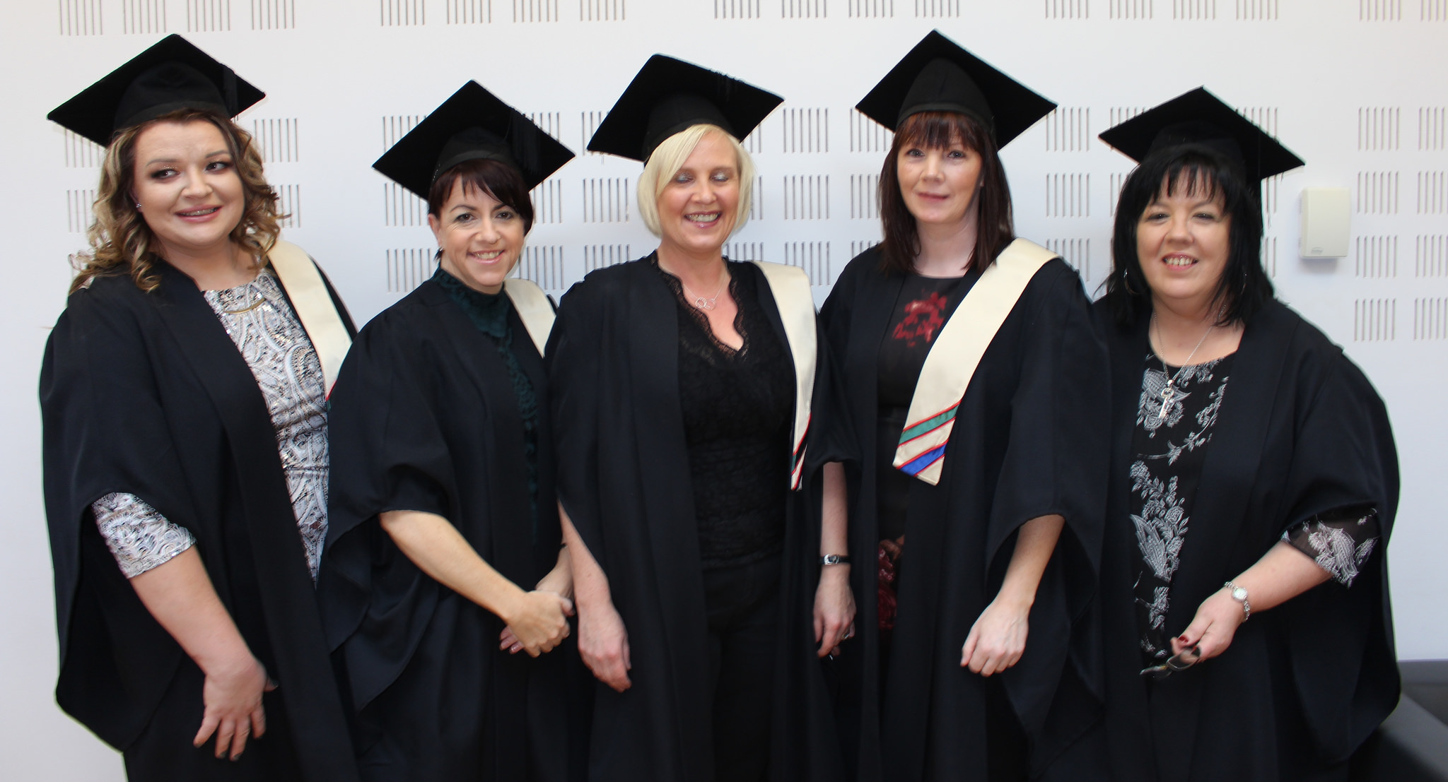 5 women smiling wearing caps and gowns graduating
