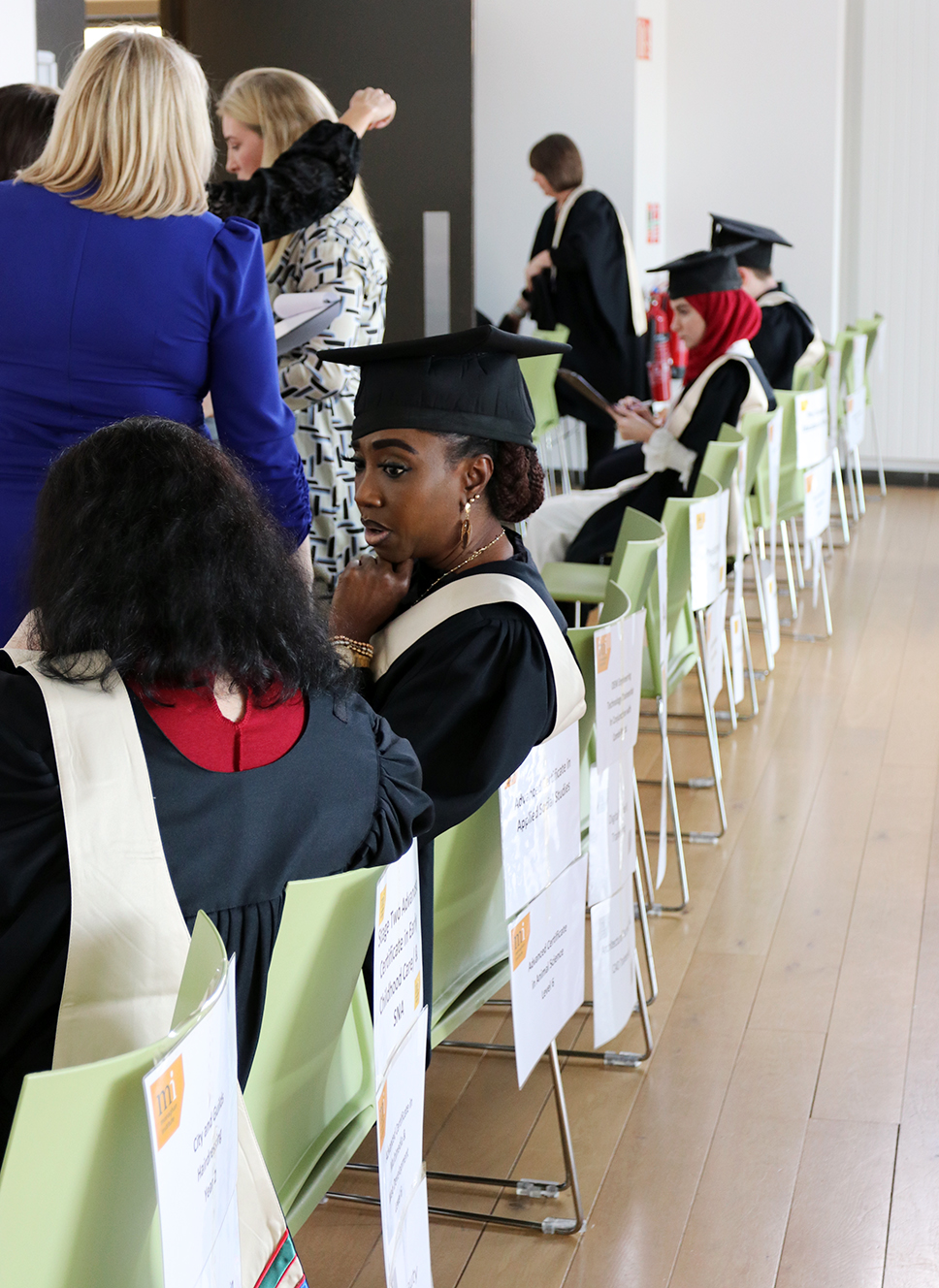 Graduation students sitting waiting on chairs with names on back of them