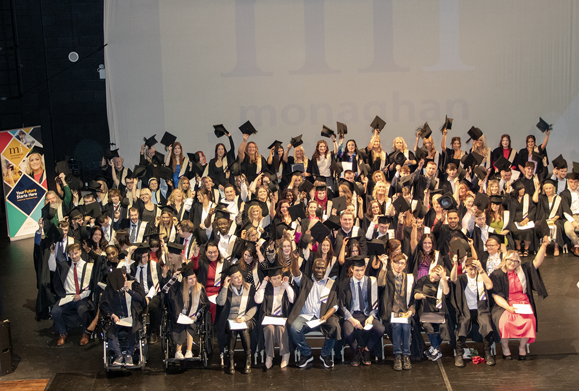 Graduating students sitting down taking caps off and raising them