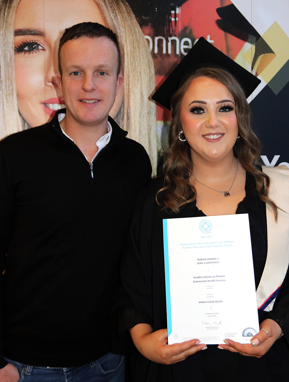 Student smiling with cap and gown holding certificate with a man smiling